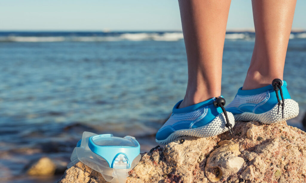 Persona in piedi su uno scoglio in riva al mare con scarpe da scoglio blu