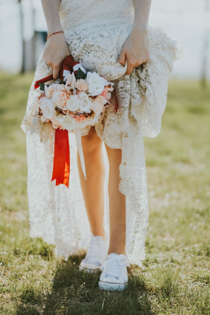Donna in abito da sposa boho con bouquet di fiori in mano e scarpe da ginnastica bianche ai piedi