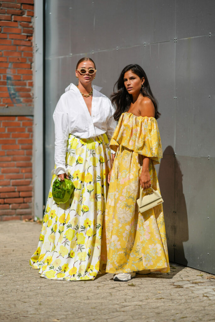 Donne in look primaverili: camicia bianca oversize con maxi gonna a fiori e abito a fiori giallo con sneakers.
